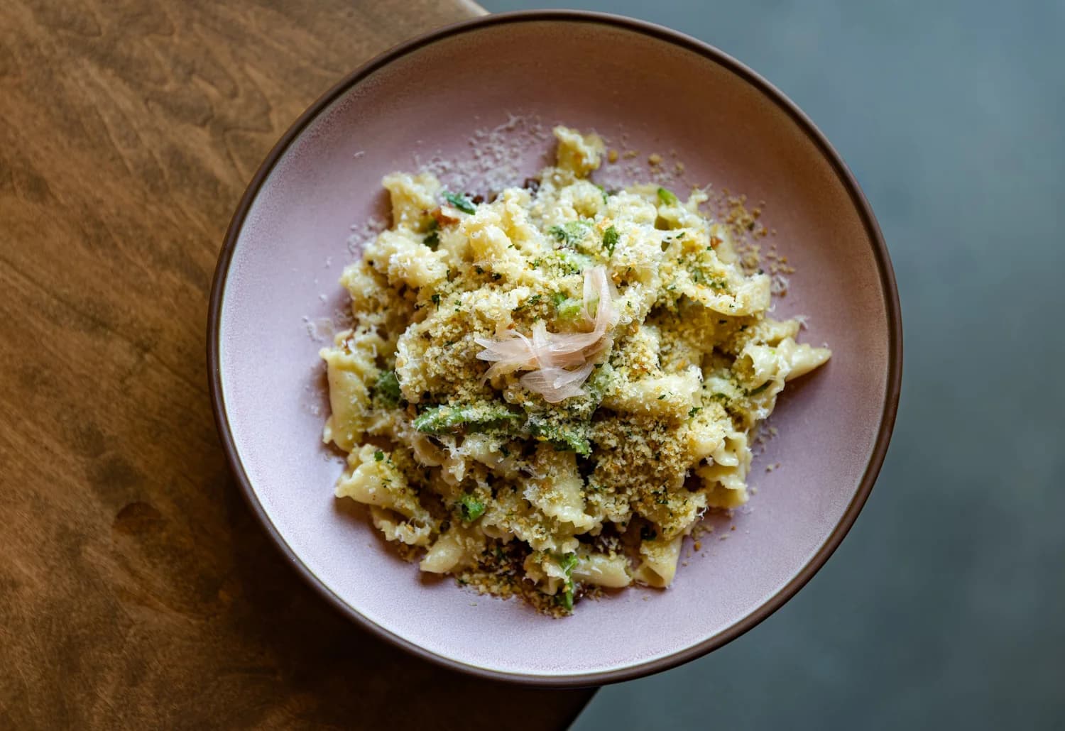 Short pasta with greens, toasted breadcrumbs and pickled shallot in a blush-pink bowl