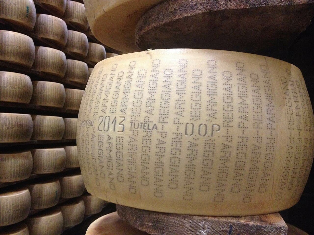 A wheel of 2013 Parmigiano Reggiano DOP stamped with its name, on the shelf of an aging room