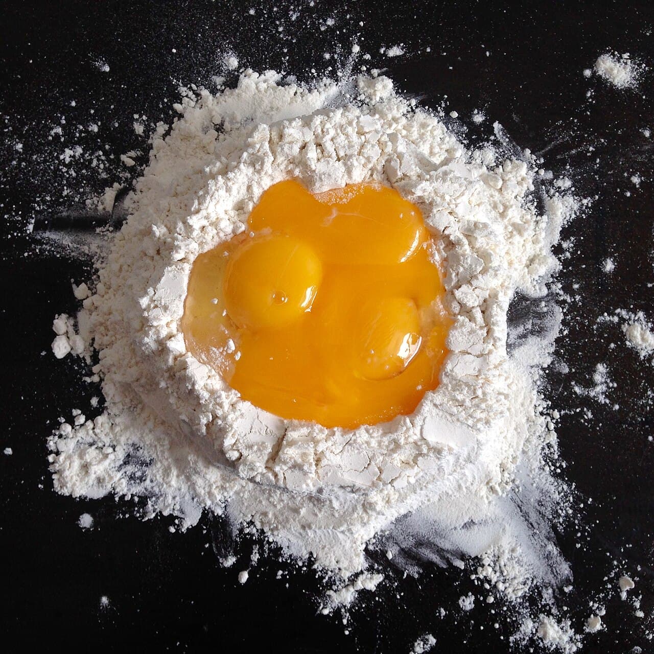 Whole eggs cracked into a well of flour on a dark surface