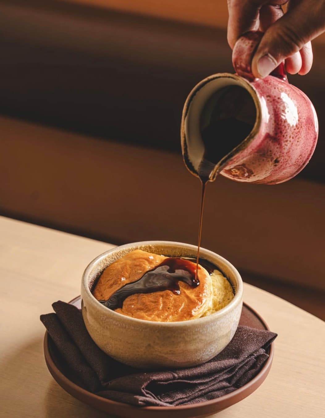 Dark vincotto poured from a ceramic pitcher over a golden soufflé
