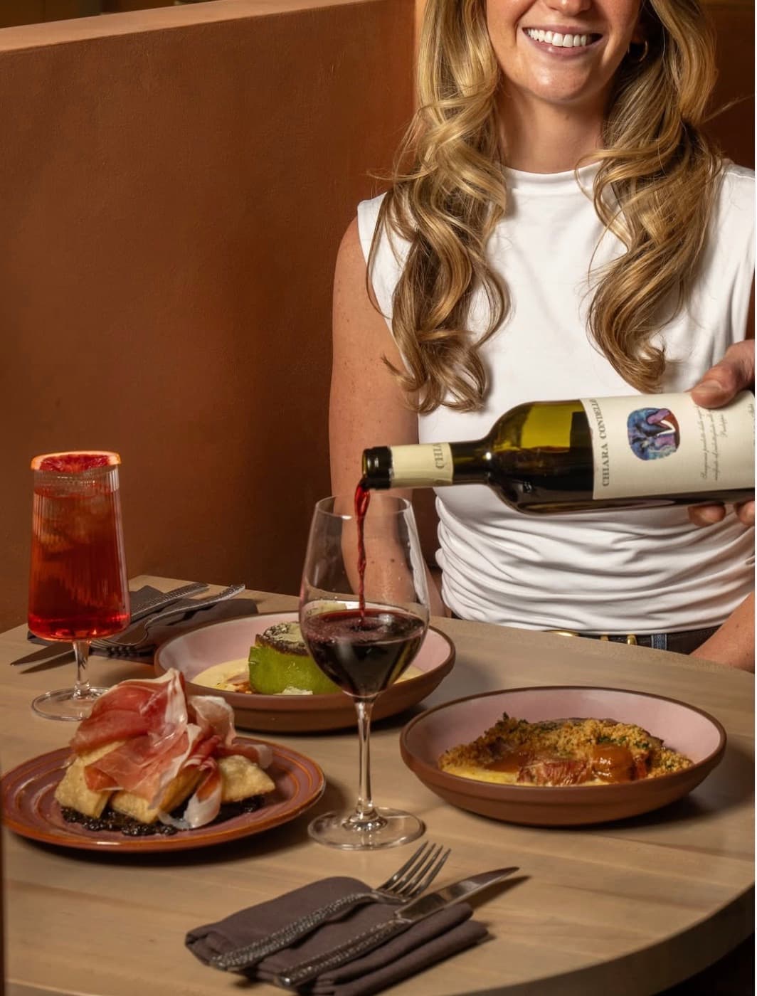 A server pouring red wine over a table of prosciutto and pasta